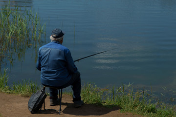 fisherman with fishing rod catching fish, sitting riverside.