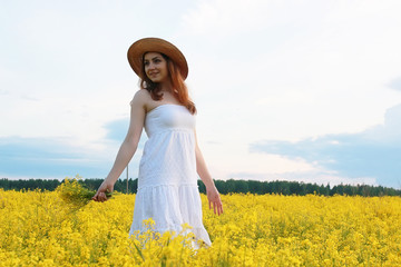 Naklejka na ściany i meble Girl in straw hat in a field of yellow flowers blossoming