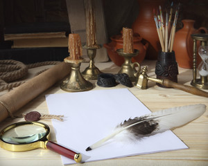 On the wooden table are: a scroll with a seal, sheets of white paper, a goose feather, an inkwell, tassels, a magnifying glass, bronze retro candlesticks with candles, old books and ceramic jugs. 
