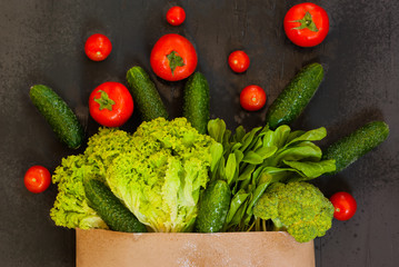 Fresh raw vegetable ingredients for healthy cooking or salad. Dark background, top view, copy space. Diet , vegetarian or vegan food. Paper bag.