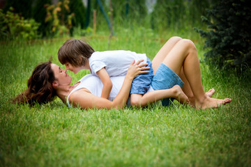 Beautiful young pregnant woman and her older child, lying down in the grass