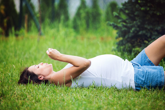 Beautiful young pregnant woman, lying down in the grass, making soap bubbles