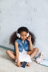 cute African girl at home, listening to music in big white headphones