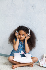 cute African girl at home, listening to music in big white headphones