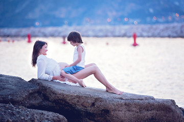 Beautiful pregnant woman, sitting on the shore on the beach on sunrise