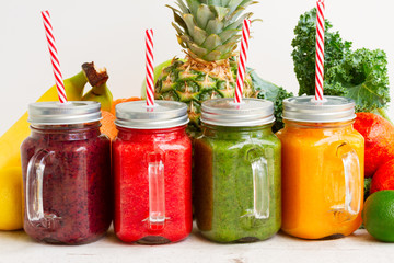 Colorful smoothie drinks with straws in glass jars with igredients close up