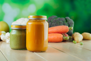 Jars with vegetable puree on the light wooden background