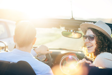 A cheerful couple drives a convertible on vacation at sunset