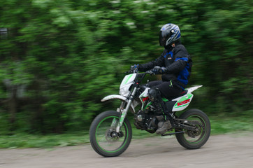 Motorcyclist in blue outfit rides against the backdrop of foliage on the off-road