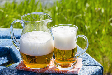 Jug and mug of beer on the table by the lake