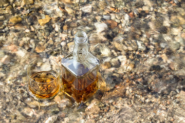 Bottle and a glass of whiskey are cooled in a mountain river