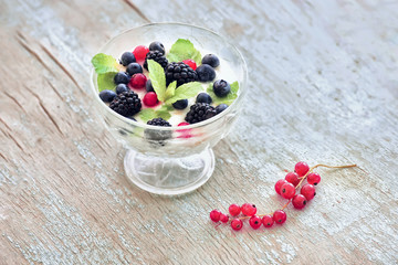 Glass plate with yogurt and various berries on an old wooden cracked light background.
