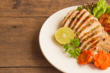 Sliced chicken breast barbecue on white plate served with grilled vegetable. Delicious  chicken breast steak and salad for dinner. Homemade chicken breast barbecue on wood table for background.