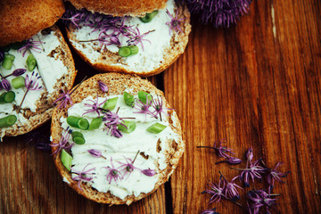 Toasted bread bruschetta with cream cheese and garlic edible flowers on olive wooden cutting board on stone slate gray background. Top view