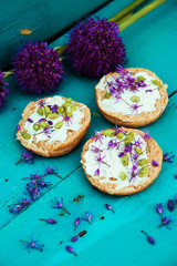 Toasted bread bruschetta with cream cheese and garlic edible flowers on olive wooden cutting board on stone slate gray background. Top view