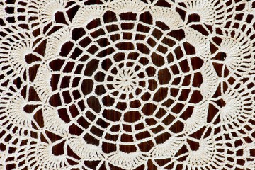 Fragment of a handmade ivory crochet on a brown wooden table