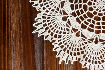 Corner of a vintage ivory crochet doily on a brown wooden table - obrazy, fototapety, plakaty