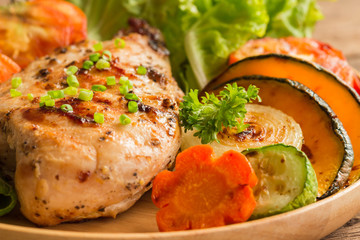 Homemade chicken breast barbecue on wood plate served with grilled vegetables. Delicious chicken barbecue and grilled vegetables for lunch or dinner. Roast chicken breast in close up concept.