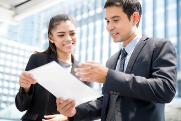 Asian businesswoman and businessman standing and discussing document