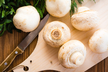 Close-up of whole fresh champignons on cutting board, parsley and knife on wooden table. Top view