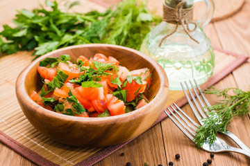 Salad made of tomatoes and fresh herbs, vegetable oil and fork on wooden table