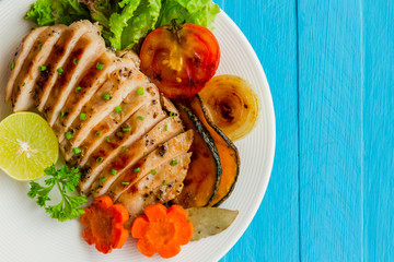 Sliced chicken breast barbecue on white plate served with grilled vegetable. Delicious  chicken breast steak and salad for dinner. Homemade chicken breast barbecue on blue wood table for background.