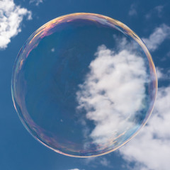 Big transparent soap bubble with sky an clouds background.