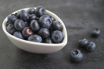 Blueberries in white bowl on the black table.