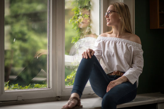 Junge Frau sitzt auf der Fensterbank und schaut nach Draussen - Ausschau halten 