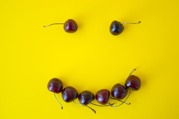 Smiley face from sweet fresh cherries. Smile sign from healthy food. Fruits on yellow background.