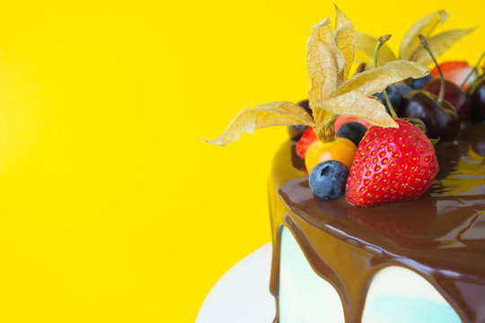 Birthday cake in chocolate with strawberries, blueberries and cherry on yellow background. Picture for a menu or a confectionery catalog.