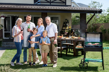 Happy family of three generations standing together on green lawn and smiling at camera