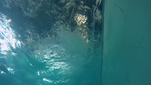 Underwater shot from bottom of pool of female athlete in cap and goggles swimming with front crawl stroke 