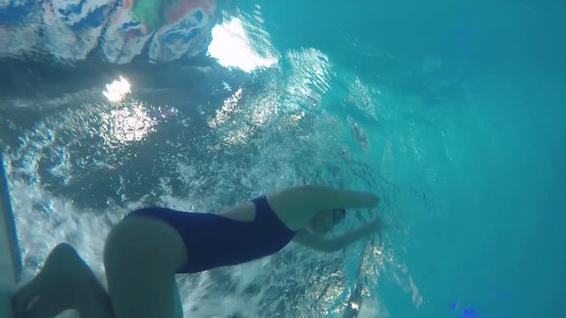Underwater shot from bottle of pool of female athlete in swimwear practicing with front crawl, then doing flip turn and swimming with butterfly stroke