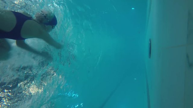 Underwater shot from side of pool of woman in swimwear practicing with front crawl, then doing flip turn and swimming with butterfly stroke