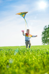 Young boy flies his kite in an open field. Little kid playing with kite on green meadow. Childhood concept.