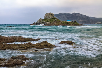 Fototapeta na wymiar Dramatic scene of rocks washes of stormy sea with small island Kastri in Kos, Greece.