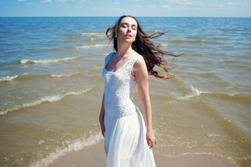 Fototapeta na wymiar Young beautiful brunette woman in white dress on the seashore