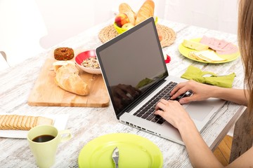 Young woman having breakfast while using a laptop computer