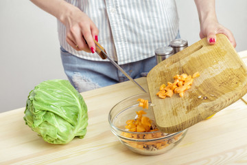 Female hands chop fresh carrot for salad on board