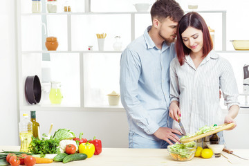 Loving happy couple preparing healthy salad of fresh vegetables in  kitchen