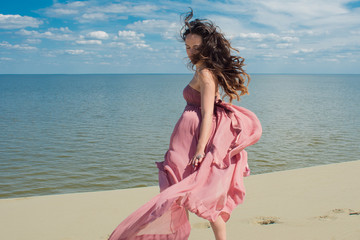 Woman in red waving dress with flying fabric runs on background of dunes. Skyline and the sea