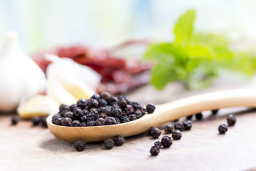 black peppercorns on wooden spoon.  closeup dried seeds.