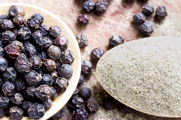 black peppercorns and black pepper powder on wooden spoon.