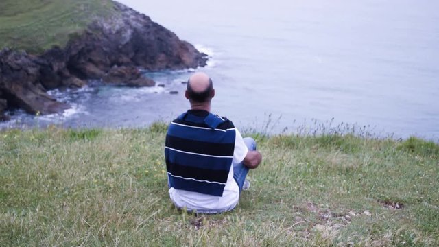 The single man sitting on a cliff looks at the ocean alone