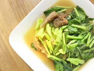 Stir-fried kale vegetable with crispy pork in white dish on the table. Thai street food.
