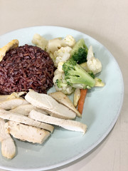 Clean food, Riceberry rice with Boiled chicken, with carrot , tometo, other vegetableand freied egg. good for you health in white dish with blur of canteen or food court background.