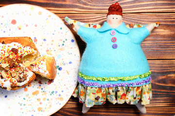Soft toy textile doll of a fat angel woman with wings next to cupcake on colorful confetti ceramic plate on wooden board. View from above. Concept of unhealthy lifestyle