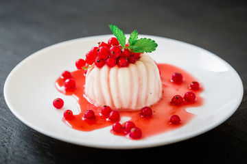 Panna cotta with fruit syrup and currant berries in white plate on a dark table. Traditional...
