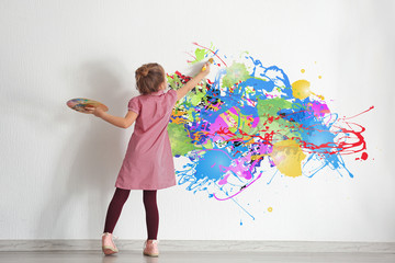 Cute little girl painting on wall in empty room